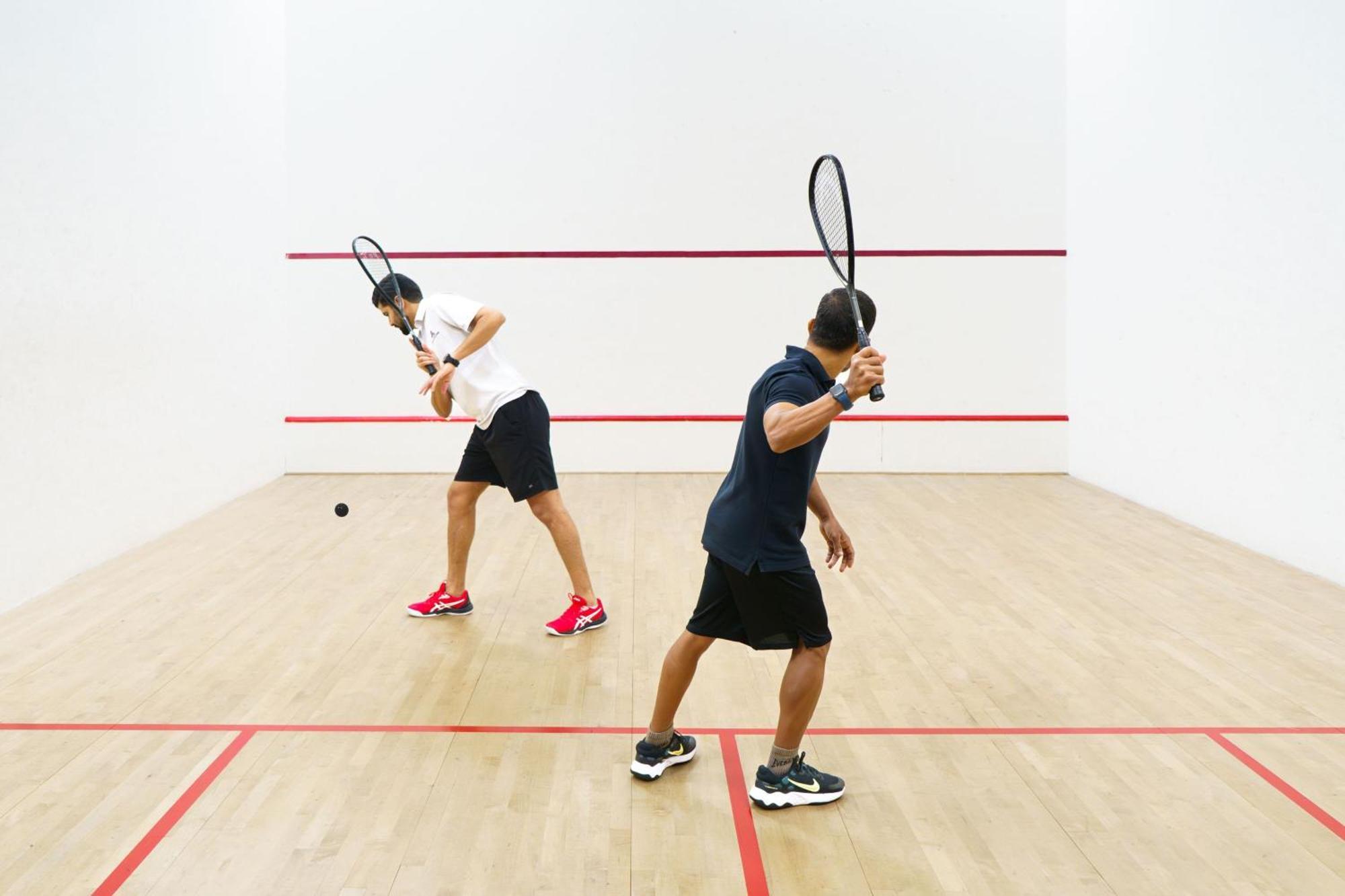 Sheraton Abu Dhabi Hotel & Resort Exterior photo The photo shows two individuals playing squash in a squash court. Each player is holding a racket and appears to be in action, with one player hitting the ball and the other preparing to return it. The court features a wooden floor and white walls, w