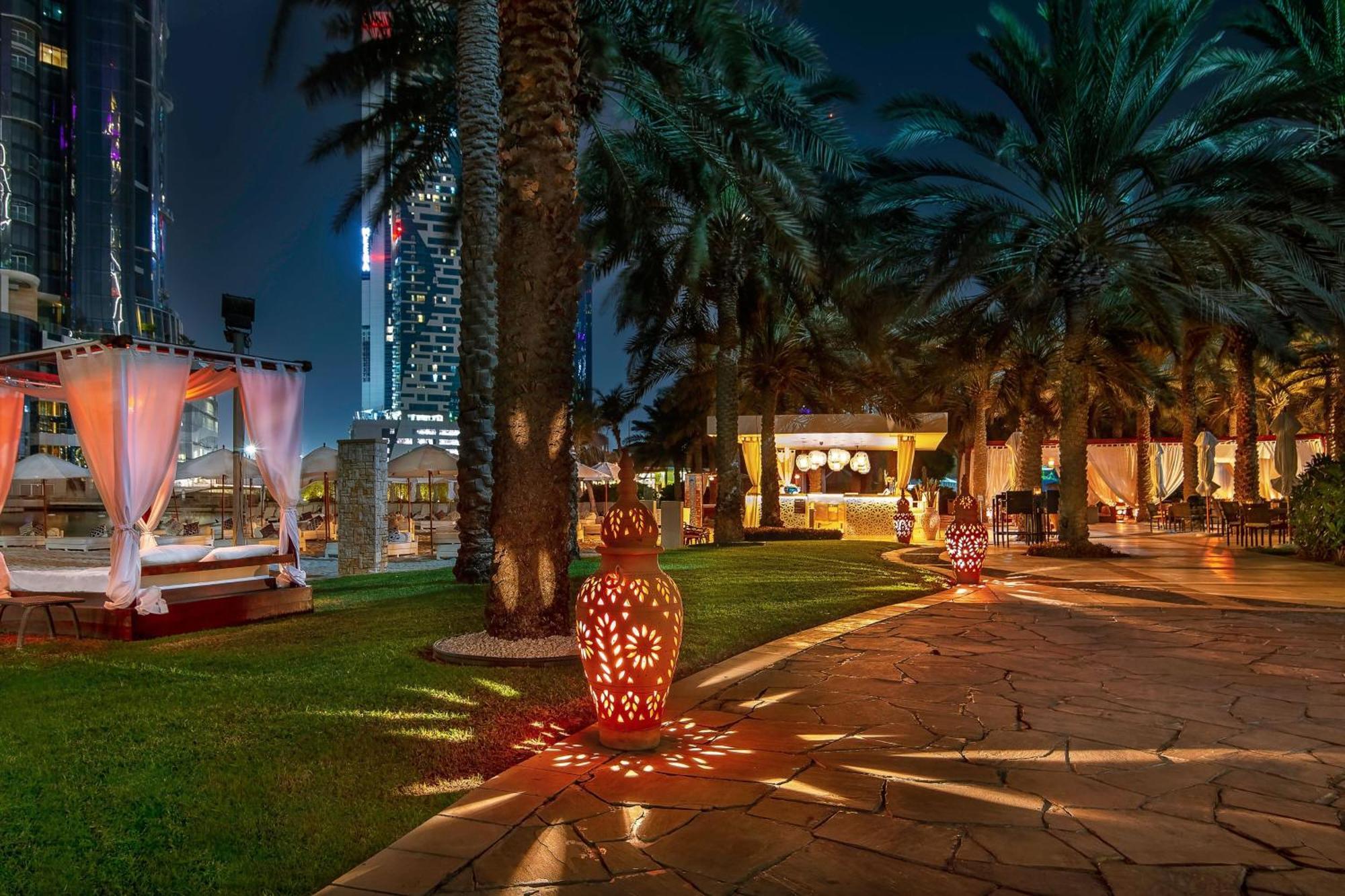 Sheraton Abu Dhabi Hotel & Resort Exterior photo The photo depicts a beautifully designed outdoor area at night, featuring palm trees and a well-maintained grassy pathway. There are decorative lanterns placed along the path, casting warm, intricate patterns on the ground. In the background, there a